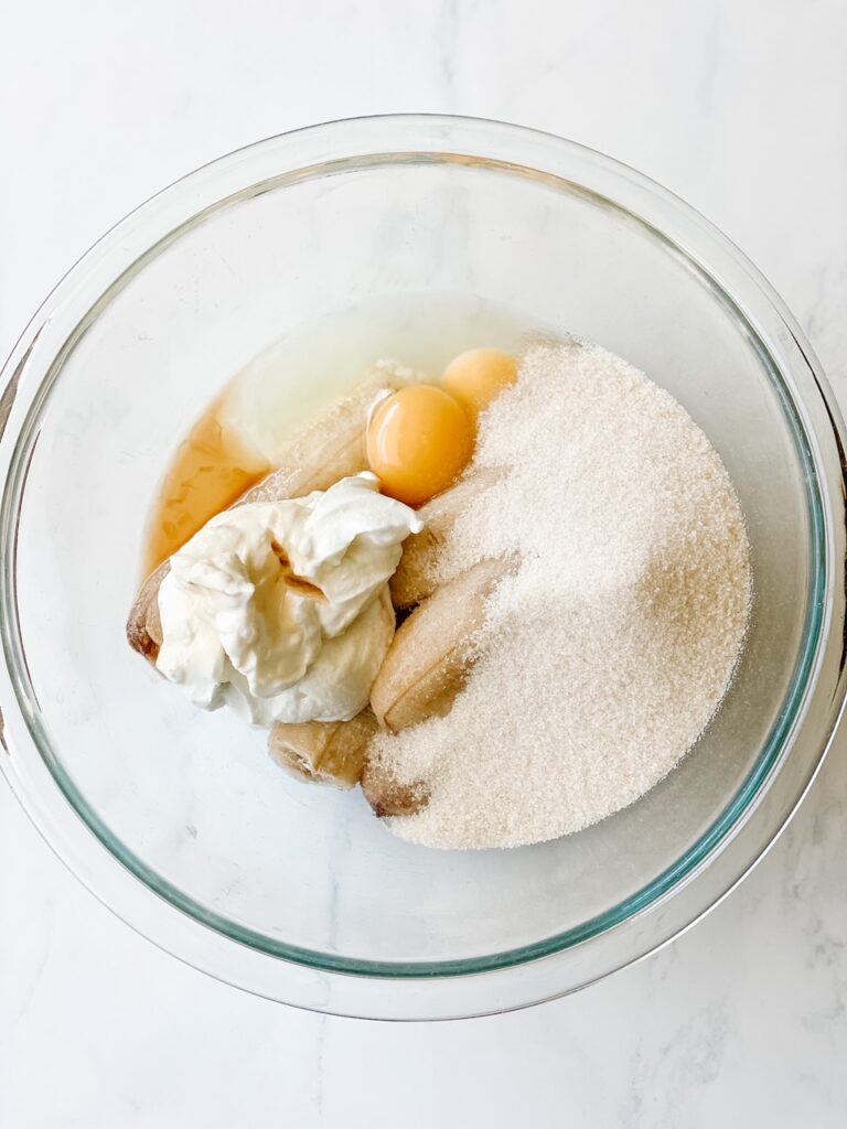 bananas eggs yogurt and sugar in a bowl for homemade banana bread with oat flour