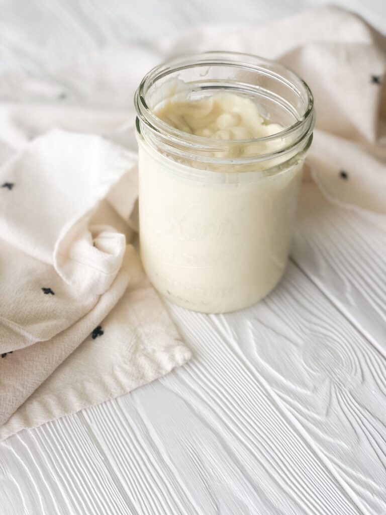 mason jar of homemade avocado oil mayonnaise with cream dish towel on white wood backdrop