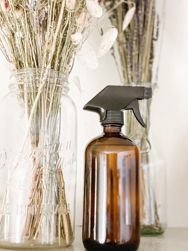 amber glass spray bottle with linen spray beside two glass jars with dried flowers