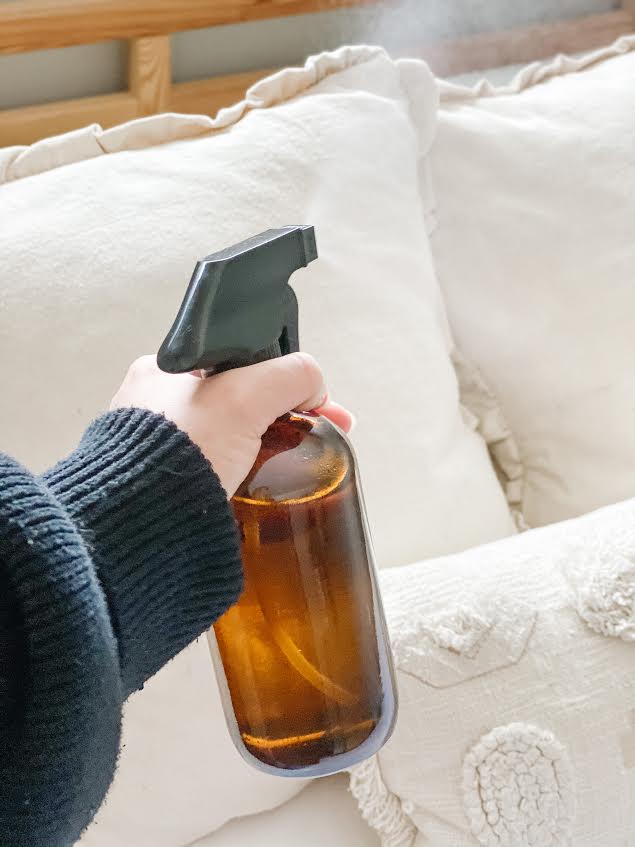 woman wearing black sweater spraying linen spray in amber glass bottle