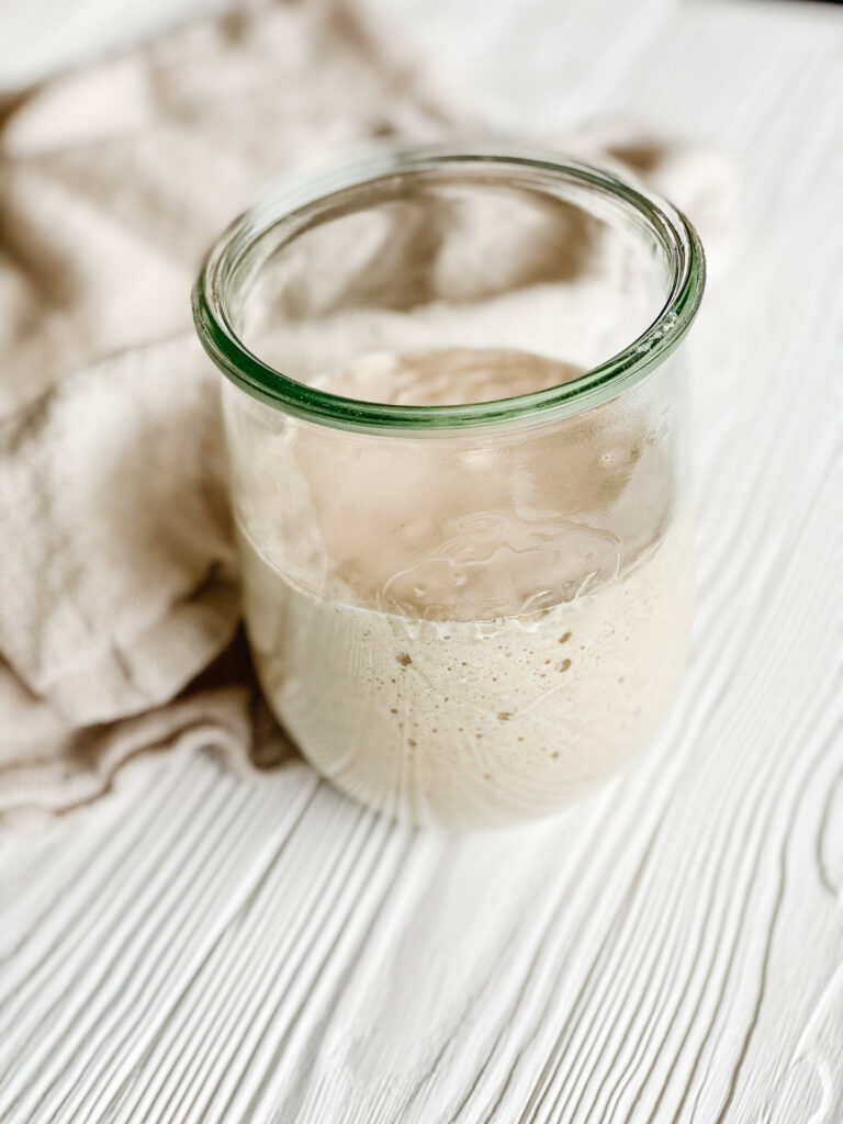gluten free sourdough starter in a glass weck jar on a white wood backdrop with a beige dish towel