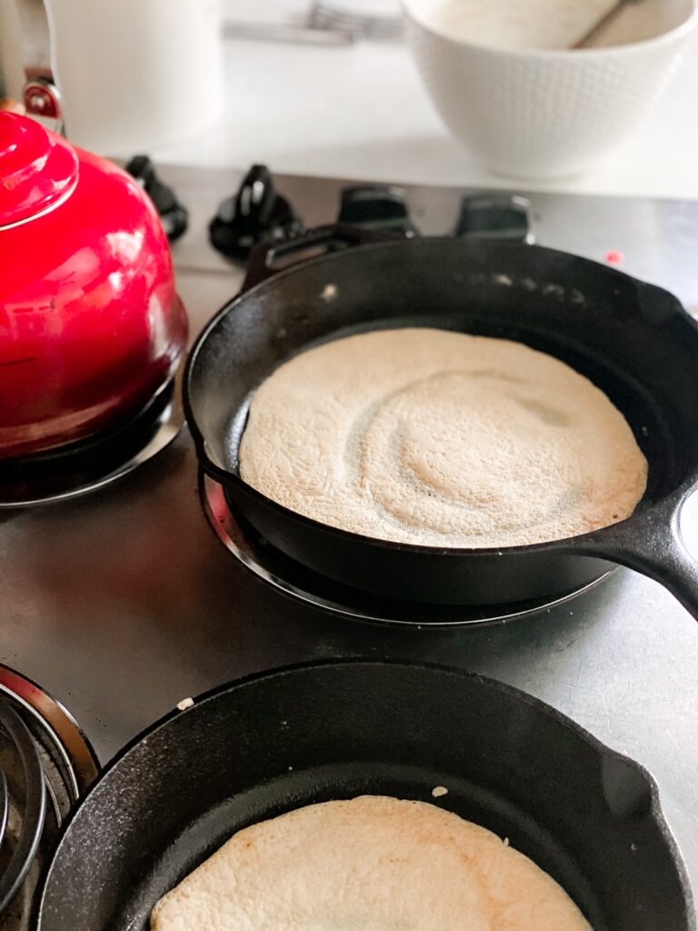 Close up shot of 2 sourdough crepes cooking in cast iron pans