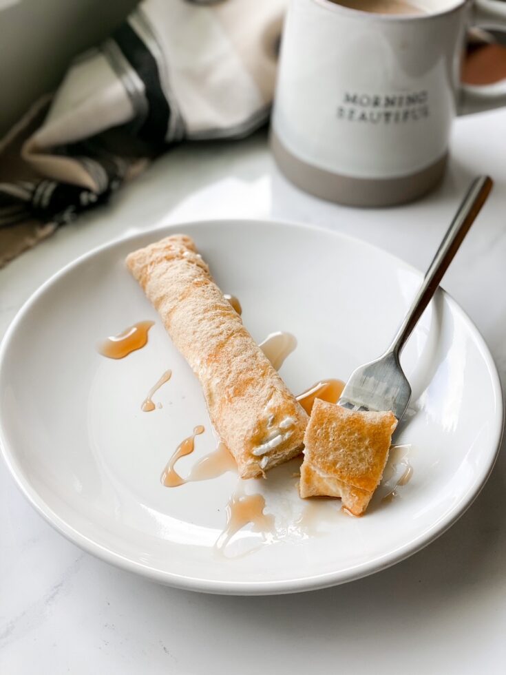 sourdough crepe with maple syrup on a white plate with plaid cloth and mug in background