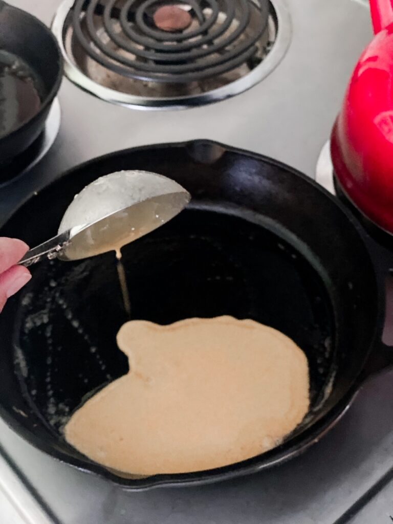 woman pouring sourdough crepe batter into a cast iron pan