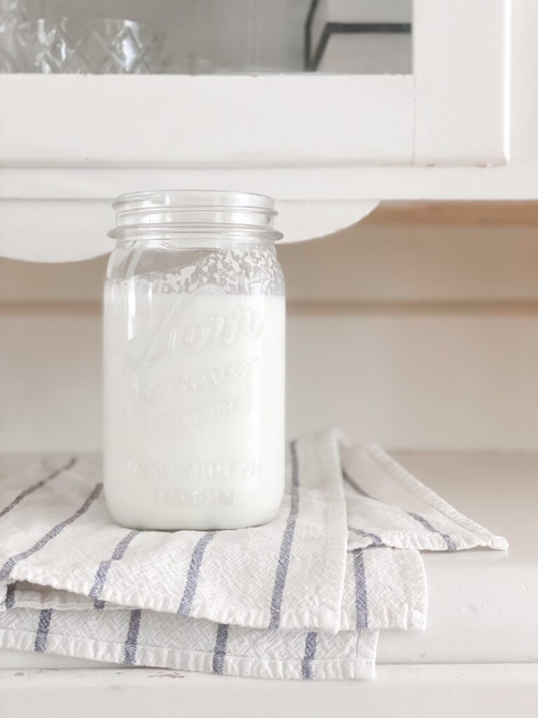 mason jar of raw milk on white and blue dish towel against cream china cabinet