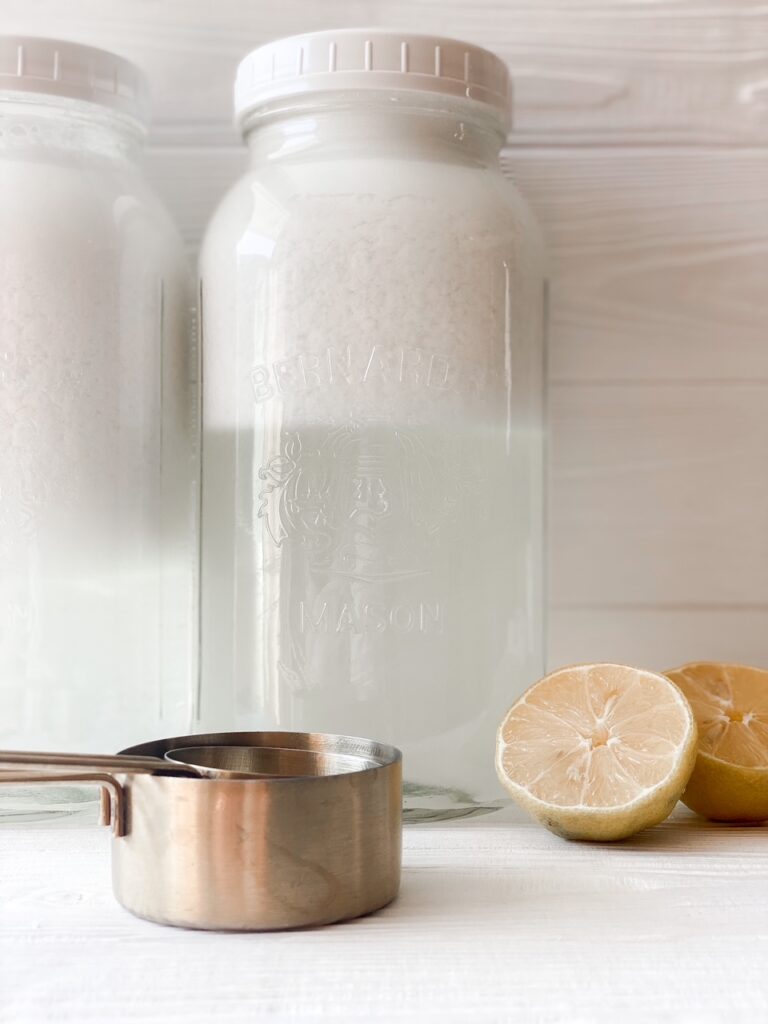 a gallon of homemade laundry detergent with a sliced lemon and measuring cups