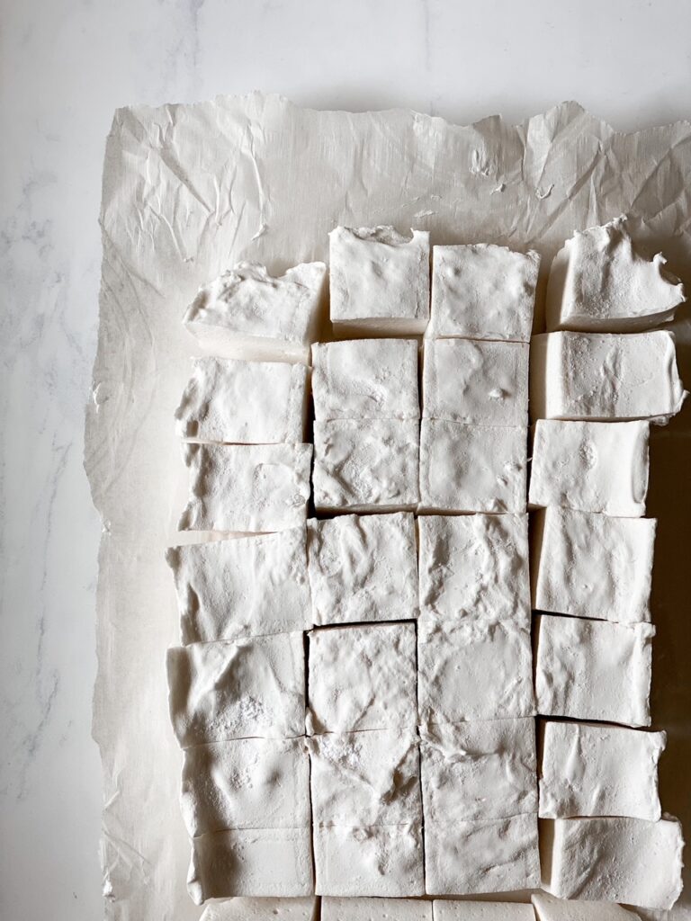 overhead shot of homemade marshmallows on parchment paper on marble backdrop