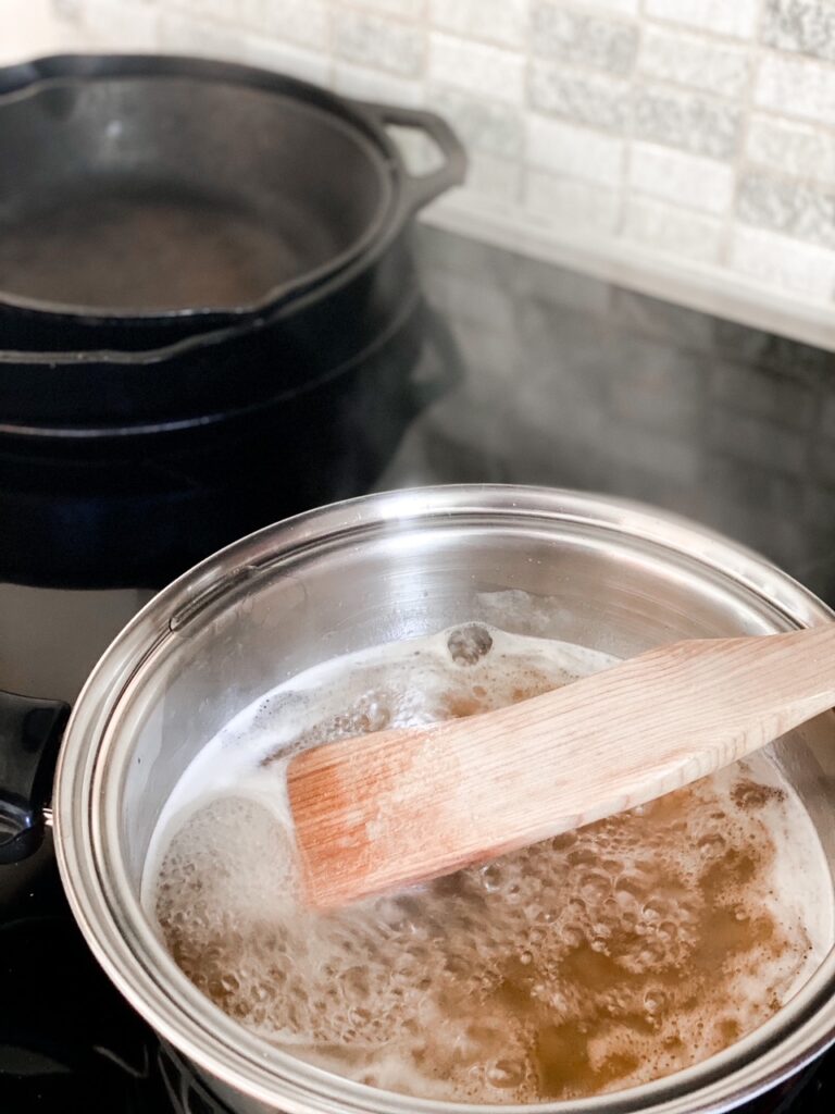 honey simmering for homemade marshmallows with a wooden spatula and cast iron pans in the background