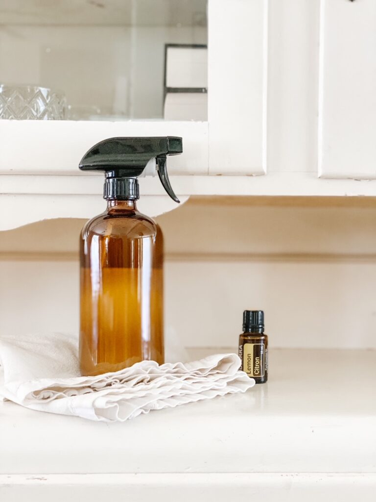 amber glass spray bottle on folded white dish cloths beside a bottle of lemon essential oil