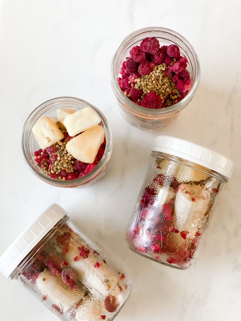 four jars of smoothie prep with bananas pineapple and raspberries