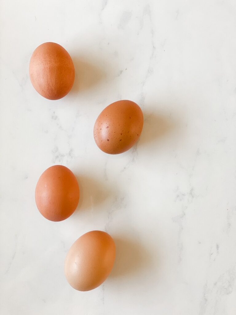 four hard boiled eggs on a white marble back drop