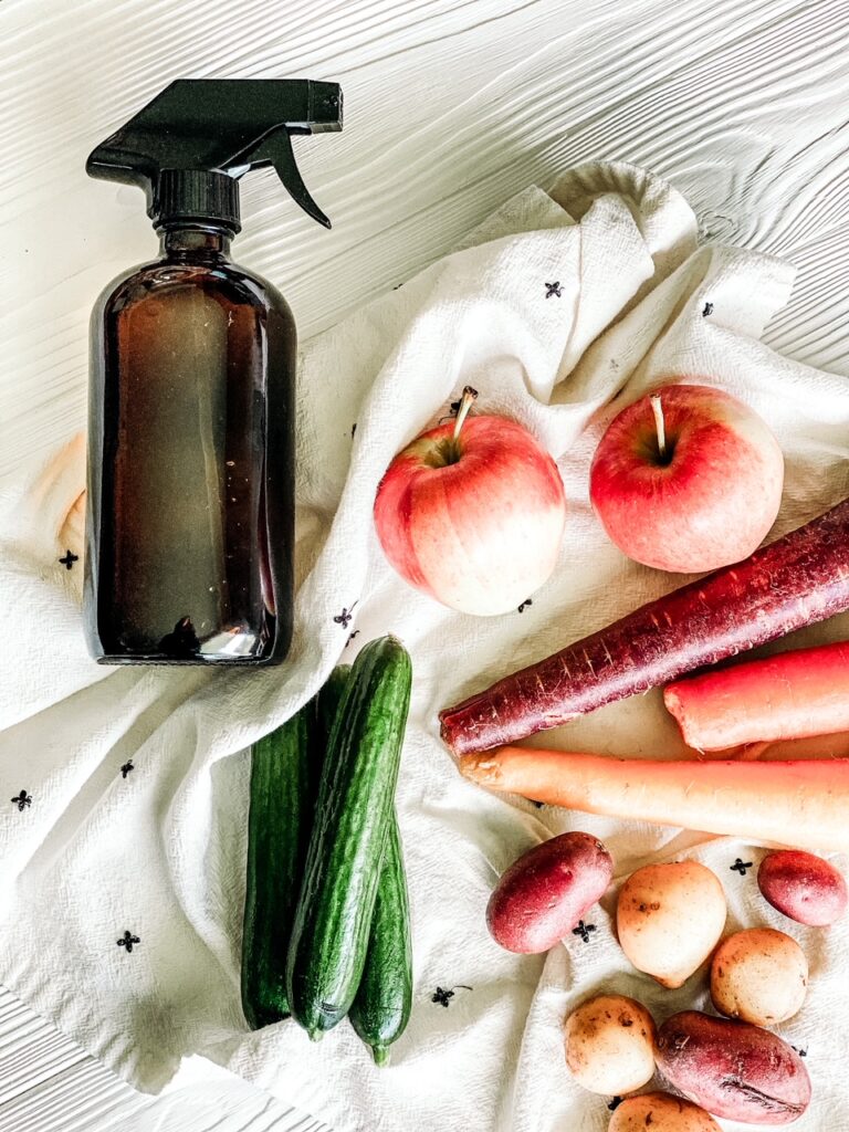 overhead shot of fruit and veggies on a white and black dish towel with amber spray bottle